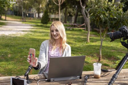 Female blond blogger interacting  her mobile - working outdoors - traveling the  influencers work...