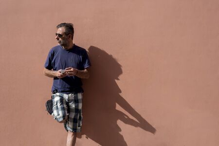 handsome Man Posing Isolated Over empty Wall Background Using his Mobile Phone on a sunny day wearing sunglassesの写真素材