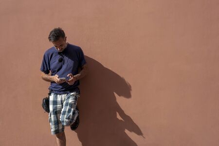 handsome Man Posing Isolated Over empty Wall Background Using his Mobile Phone on a sunny day wearing sunglassesの写真素材