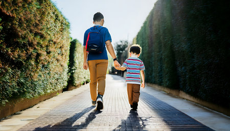A heartwarming image of a father and son walking hand in hand on a picturesque pathway lined with lush green hedges, capturing a moment of bonding and togetherness.の素材