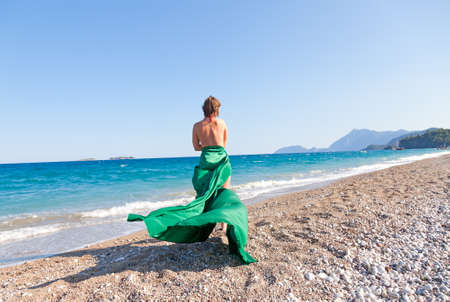 Beautiful girl silhouette with green tissue posing on the mediterranean sea beachの写真素材