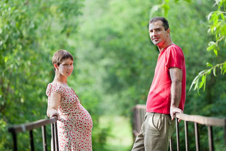 Husband with his pregnant wife on the bridge in green forestの写真素材