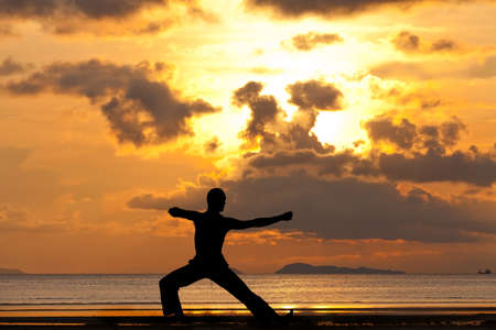 Man silhouette doing yoga exercise archer at sunset beachの写真素材