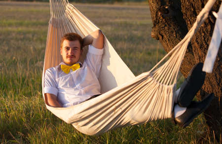 Young man swinging in hammock at sunset