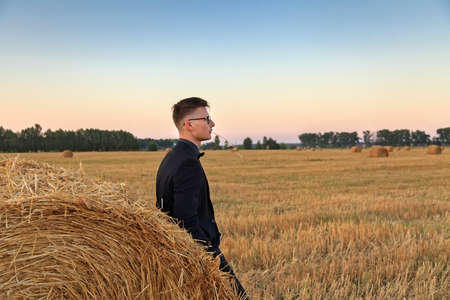Young man with glasses thinking and standing on the fieldの写真素材