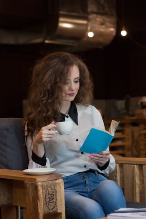 Beautiful girl with coffee reading a book in a coffee shopの写真素材