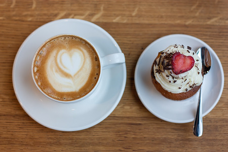 Cup of cappuccino and cupcake on wooden tableの写真素材