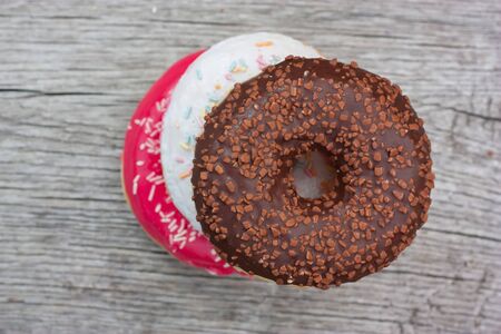 Three colorful donuts facing each other on a wooden tableの写真素材