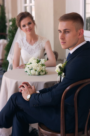 The groom looks at the camera while sitting at a table with the brideの写真素材