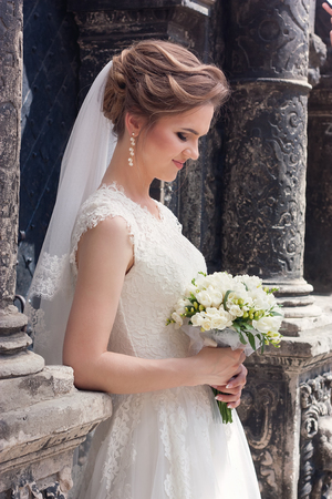 Young bride with wedding bouquet stands near a beautiful old wallの写真素材