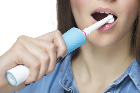 Close up of brushing teeth with electric toothbrush. Young woman. Isolated on white backgroundの写真素材
