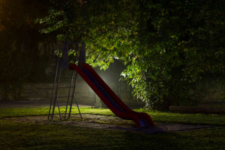 An empty playground with a red slide at night with fog and creepy atmosphereの写真素材