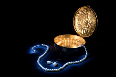 An old beautifully engraved silver box with pearl jewels on black tissue. Light painting with...