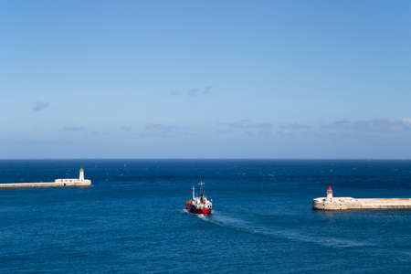 A red ship passes the two lighthouses in front of the old town of Valletta, Malta.の写真素材