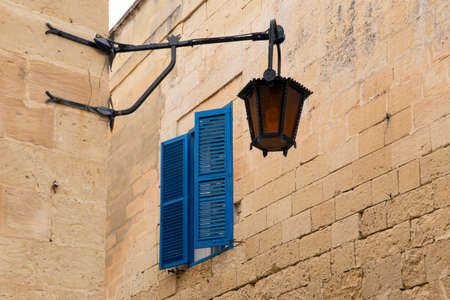 A narrow street in the historical medieval city of Mdina on Malta. View on blue window panes and a street lamp.の写真素材