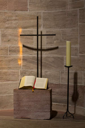 An alcove for prayer in a church with metal cross, candle, book and golden reflection from a window
