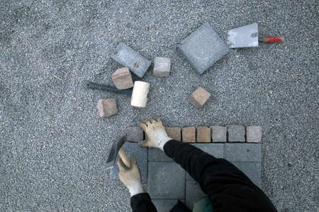 Working on a stone path in the garden. Top view on a garden worker using stones and hammer on grey gravelの写真素材