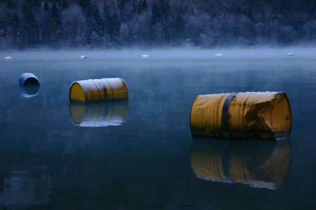 Rusty old oil barrels as buoys on a cold lake in winter covered with frostの写真素材