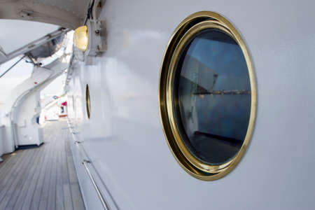View of a round porthole with golden rim on board of a white painted luxurious yachtの写真素材