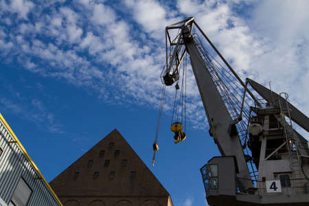 A grey painted dock side crane at a river port in front of an old brick storage building.の写真素材