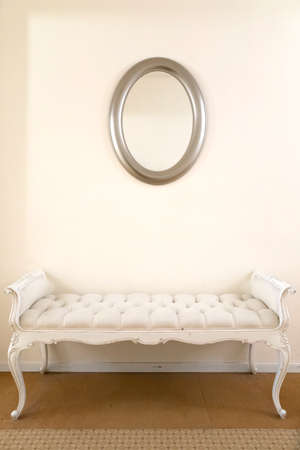 A white luxurious vintage couch underneath a simple mirror.の写真素材
