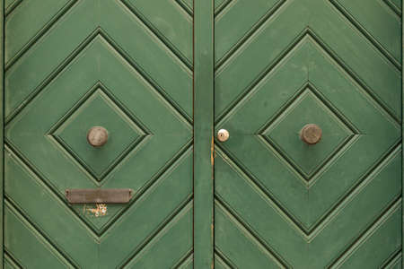 A green painted wooden double door with diamond pattern and round door knob. The left door side has a slit for mail.の写真素材
