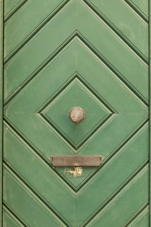 A green painted wooden door with diamond pattern, round door knob and a mail box.の写真素材