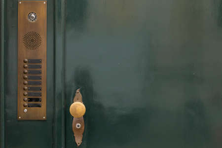 A dark green painted door with bronze door bells and a golden round door knob. Free space on the right side of the image.の写真素材