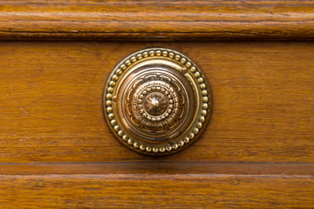 A beautiful round golden door knob with ornaments. Brown wooden door in the background.の写真素材