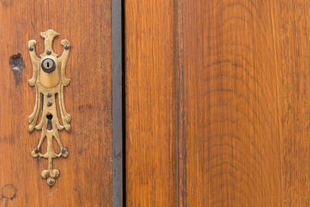 Closeup of a brown wooden door with an intricate key hole decoration in form of a bird.の写真素材