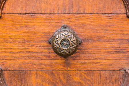 Closeup of the ornament metal knob of a brown wooden door.の写真素材