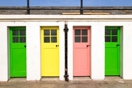 A storage house with white walls and colored narrow doors in plain sunlightの写真素材