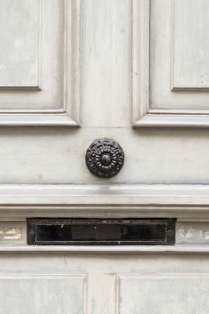 A grey painted wooden door with black, round door knob and black mail box slit. Closeup with central view.の写真素材