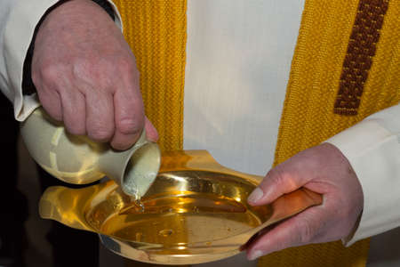 A priest pours holy water from a ceramic jug into a golden plate during a christening ritualの写真素材