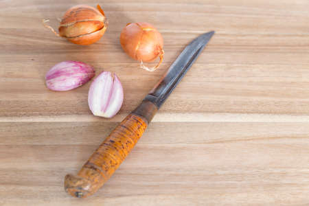 Close view on a brown wooden cutting board with a big knife, two unpeeled onions and a peeled and cut onionの写真素材