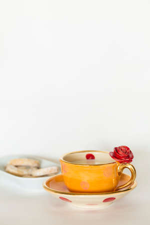 A beautiful orange golden cup with red rose ornament and milk and delicious cookies on a white plateの写真素材