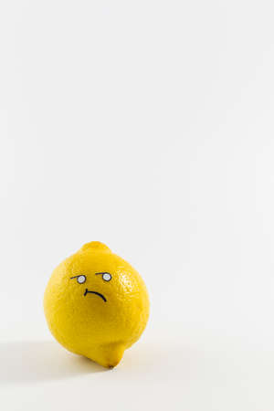 A fresh yellow lemon with sour looking cartoon style face on white backgroundの写真素材