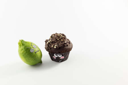 A sweet chocolate muffin and fresh lemon with cartoon style faces on white background opposing each otherの写真素材