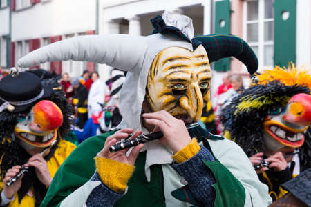 Basel carnival. Nadelberg, Basel, Switzerland - March 7, 2017. Closeup of a single participant with a clown mask and a green and white costume playing piccolo.のeditorial素材