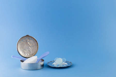 Baby boy luxurious items collection isolated on pale blue background. Hairbrush and comb in a silver can, pacifier on a silver plate.の写真素材