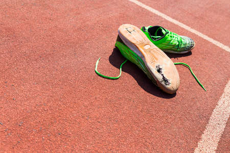 A pair of broken green running shoes with big holes in the sole laying on a running trackの写真素材