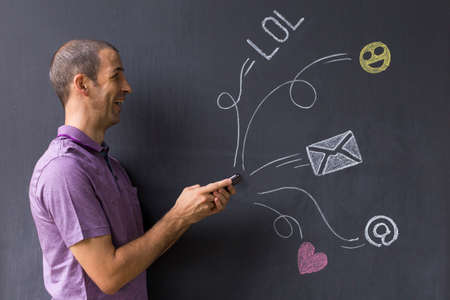 Concept of social media chat. Single white adult man standing in front of a blackboard using his...