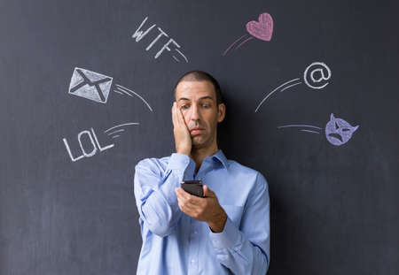 Concept of social media chat. Single white adult man standing in front of a blackboard using his...