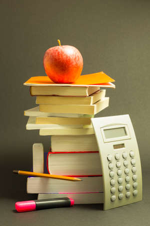 Concept of education. Stack of school books with calculator, pink marker and pencil and a red apple...
