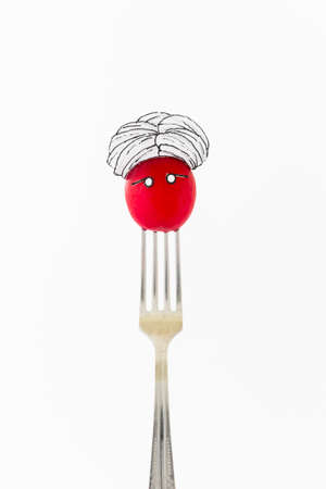 Single red radish on white background with turban sitting as a fakir on top of a silver fork representing indian food.の写真素材