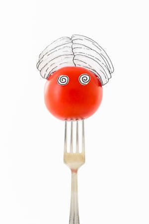 Single red tomato on white background with turban sitting as a fakir on top of a silver fork representing indian food.の写真素材