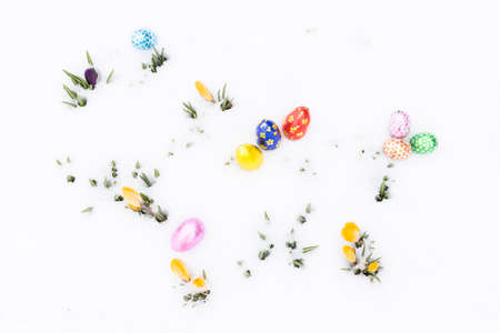 Top view on chocolate easter eggs wrapped in pink, orange, green, golden, blue and red aluminum foil laying on fresh snow besides young yellow crocus buds outdoors in springの写真素材