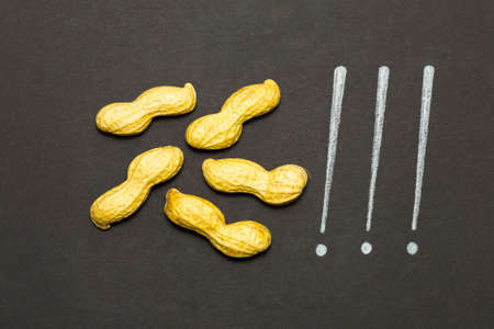 Concept of the saying that's peanuts! Raw unpeeled peanuts and white pencil hand writing on black paper backgroundの写真素材