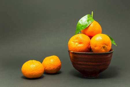 Still life studio shot of a red ceramic bowl with black texture filled with fresh orange tangerines on gray background.の写真素材