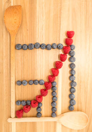 Statistical line curve graph made of kitchen spoons, fresh blueberries and raspberries on a brown wooden cutting boardの写真素材